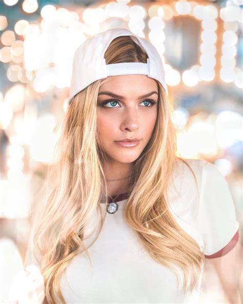 A Woman With Long Blonde Hair Wearing A White Shirt And Hat In Front Of Lights
