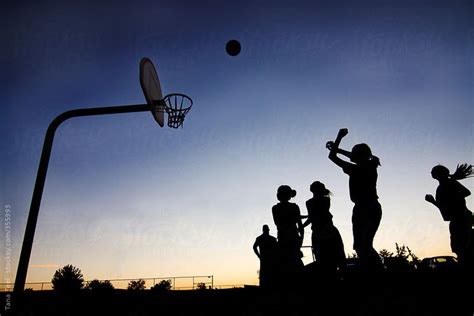 Silhouettes Of People Playing Basketball At Sunset By An Object Flying