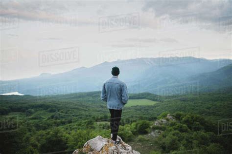 Man Standing On Cliff By Mountain And Forest Stock Photo Dissolve