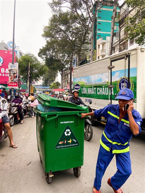 A Garbage Man Pulls The Trash Can At A Busy Street In Ho Chi Minh