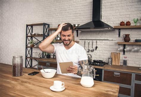 Young Handsome Man Is Having His Breakfast Cereals With Milk At The Kitchen And Reading Morning