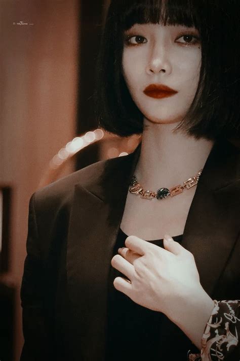 A Woman With Black Hair Wearing A Suit And Red Lipstick Holding Her