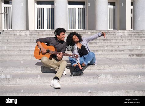 A Young Latin Couple Playing The Guitar And Making A Selfie Sitting On