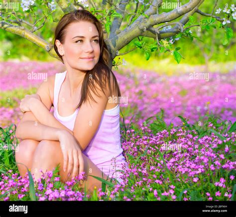 Portrait Of Beautiful Calm Girl Sitting Down On Pink Floral Glade Under