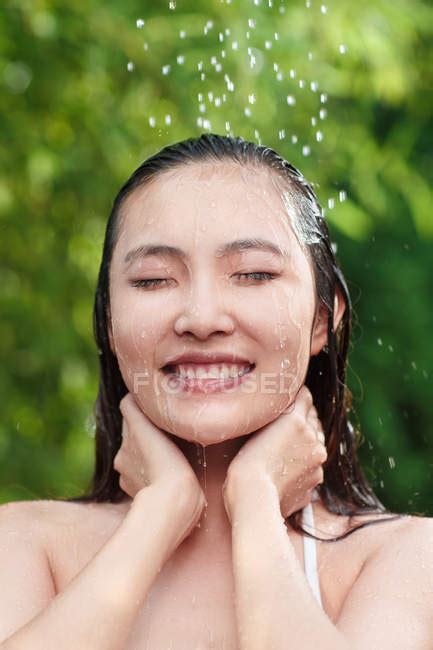 Attractive Smiling Young Asian Woman With Closed Eyes Taking Shower On Green Natural Background