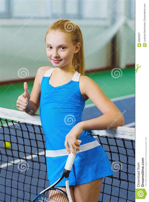 Милая девушка играя теннис и представляя или выставка большой палец руки вверх в суде крытом