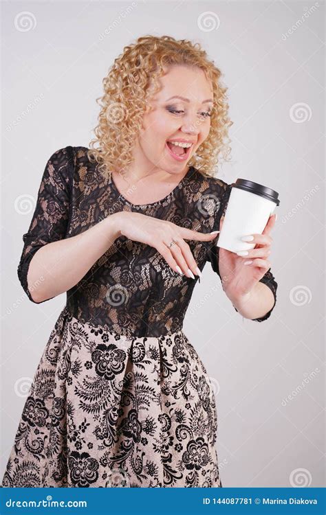 Cute Curly Blonde Girl Stands In Lace Short Evening Dress And Holds A Paper Cup Of Coffee On A