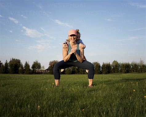 Happy Mother Carrying Daughter While Exercising On Grassy Field At Park