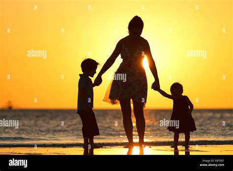 Siluetas De Una Madre Y Sus Dos Hijos En La Playa En El Atardecer