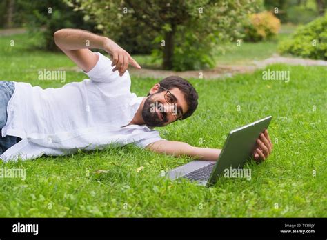 Young Man Working On His Laptop While Lying On The Grass Of The Park Happy Expression Concept