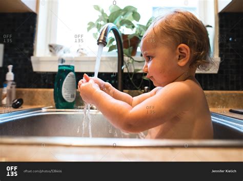 Baby Playing With Water While Getting A Bath In The Kitchen Sink Stock