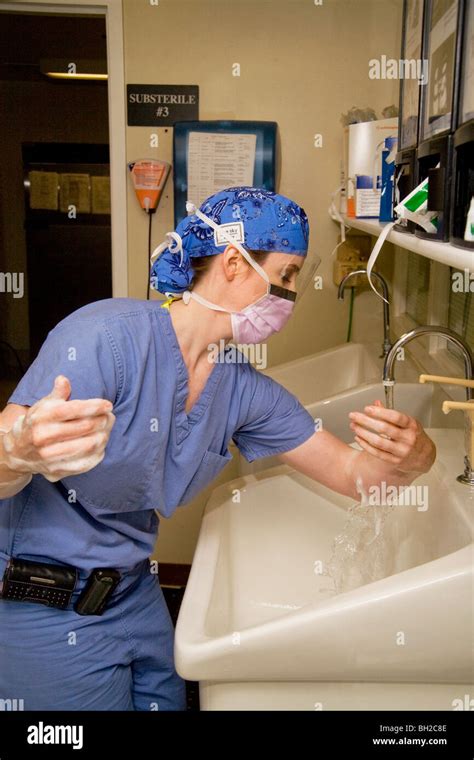 Dressed In Scrubs And Wearing A Surgical Mask A Woman Surgeon Washes