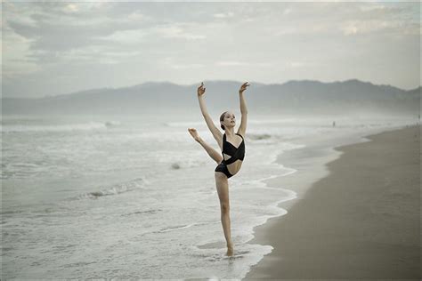 A Woman In A Black Leotard Standing On The Beach With Her Arms Up