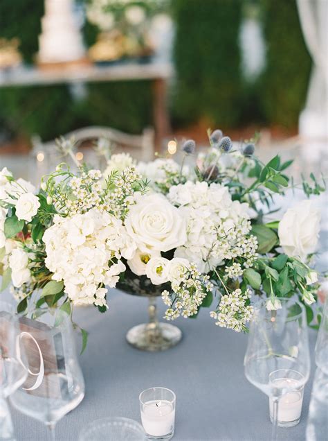 White Flowers And Greenery Are Arranged In Clear Vases On A Blue Table