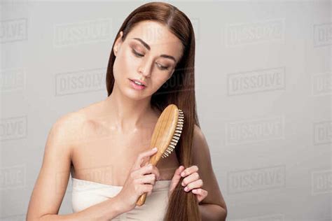 Attractive Brunette Girl Combing Hair With Natural Wooden Hairbrush Isolated On Grey Stock