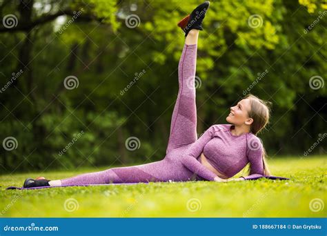 Fitness Woman Working Out And Stretching Legs While Sitting On Exercise Mat In Green Park Stock