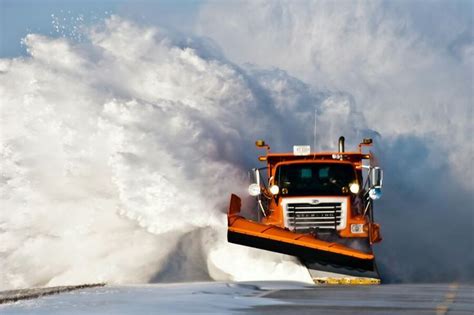 A Snow Plow Clearing The Road In Front Of A Huge Wave