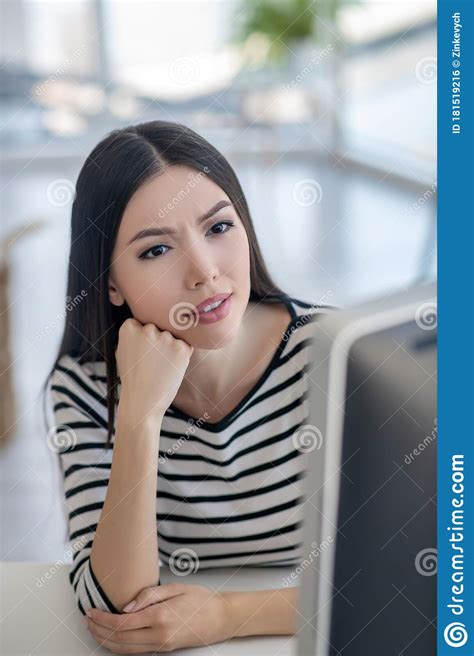 Brunette Woman In A Striped Shirt Listening Carefully Stock Photo