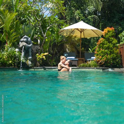 happy couple kissing while relaxing in outdoor spa infinity swimming pool surrounded with lush