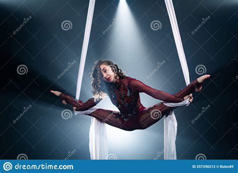 female athletic and flexible aerial circus artist dancing with aerial silk on the stage stock