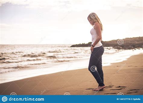 Lonely Beautiful Blonde Young Woman Walking On The Shore With Nude Feet On The Sand At The Beach