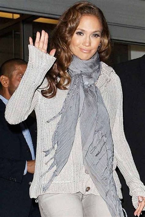 The Woman Is Waving Her Hand And Wearing A Gray Scarf Around Her Neck