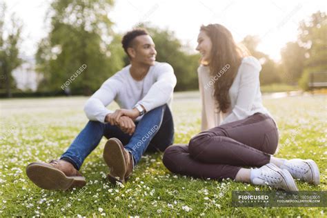 Young Couple Sitting On Grass Face To Face Smiling — Lens Flare Female
