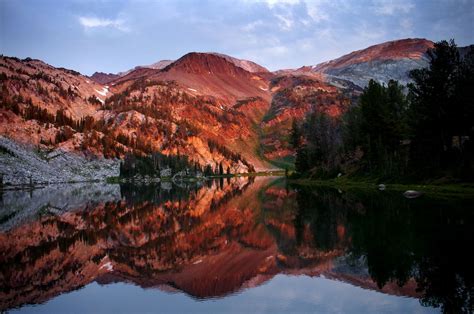 The Mountains Are Reflected In The Still Water At Sunset With Trees