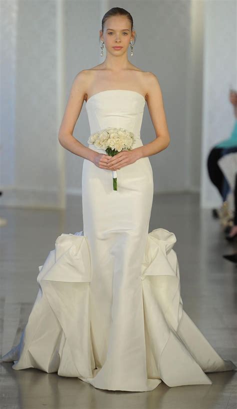 A Woman In A White Wedding Gown Holding A Bouquet Of Flowers On The Catwalk