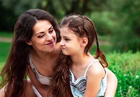 Beautiful Playful Mother Embracing And Talking With Her Cute Angry Daughter On Summer Green