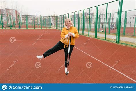 An Elderly Woman Holding A Nordic Walking Stick Stands On The Red
