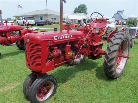Two Red Farmall Tractors Are Parked On The Grass In Front Of Some Other