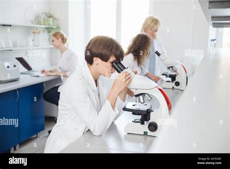 Researcher Using Microscope With Colleagues Working In Background Stock