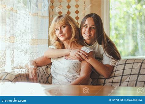 Loving Adult 20s Daughter Hug Elderly Mother From Behind While Mom Sitting On Couch People