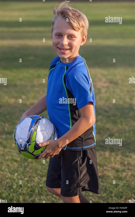 Portrait Of Boy Football Player Holding Football On Practice Pitch