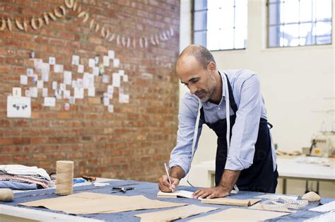 Male Fashion Designer Working At Table In Workshop Stock Photo