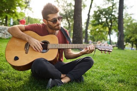 평온한 주말을 보내고 잔디에 앉아 공원에서 기타를 연주 잘 생긴 웃는 남자 무료 사진