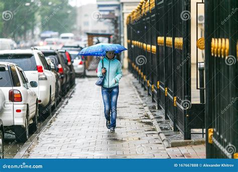 People Walk Under Umbrellas During Light Rain On The Wet Streets Of The