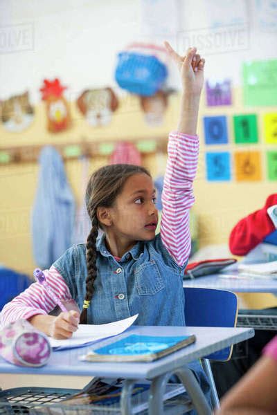 Primary Schoolgirl With Hand Raised In Classroom Stock Photo Dissolve