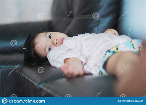 Asian Toddler Girl Laying Down On Dark Brown Sofa With Sad Eyes