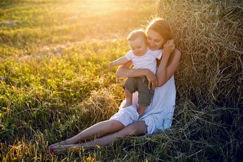 Молодая девушка в белом платье сидит со своим сыном из стога сена во время — Стоковое фото ...