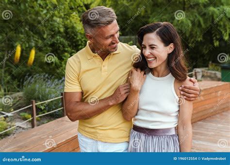 Portrait Of Smiling Middle Aged Couple Laughing And Hugging While Walking In Summer Park Stock