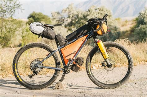 An Orange And Black Bicycle Parked On The Side Of A Dirt Road With