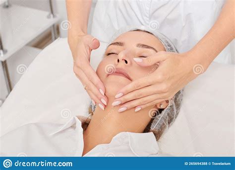 beautician massages woman face skin after rubbing moisturizing cream for rejuvenation in clinic
