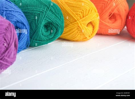 Many Multi Colored Balls Of Threads On Knitted Fabric On White Wooden