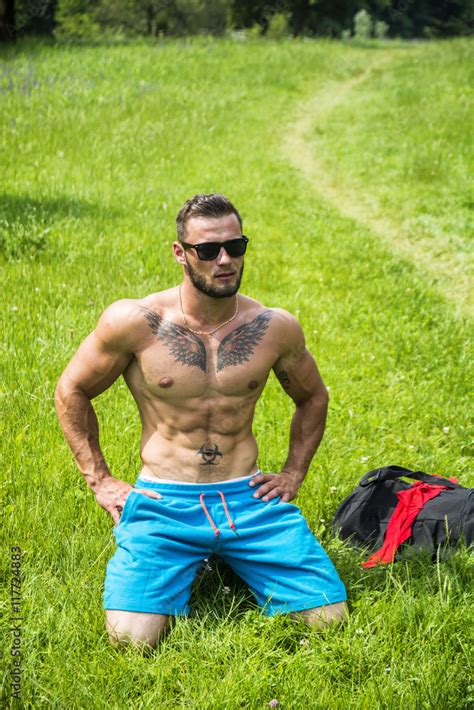handsome muscular shirtless hunk man outdoor in city park sitting on grass showing healthy