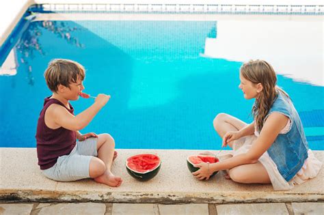 Outdoor Summer Portrait Of Two Funny Kids Eating Watermelon By The Pool
