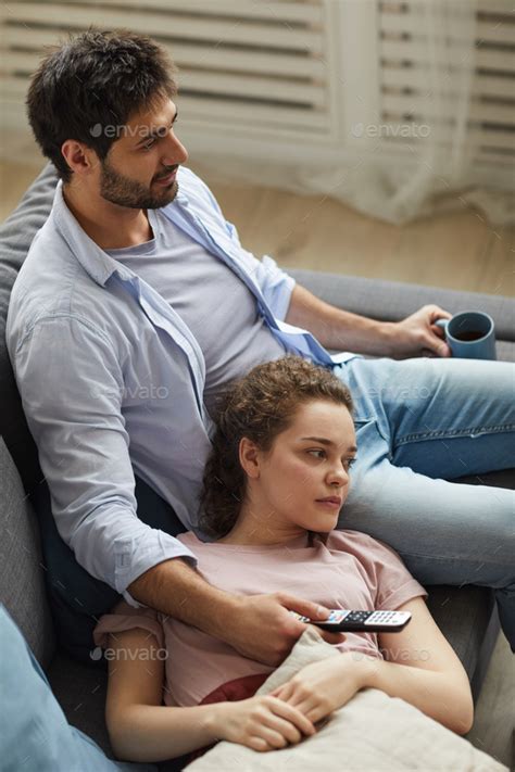 Couple Relaxing On Sofa At Home And Watching Tv Stock Photo By