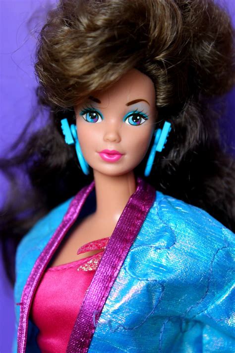 A Close Up Of A Barbie Doll Wearing A Blue Jacket And Pink Dress With Large Earrings