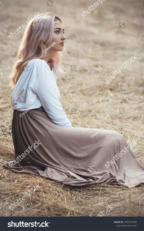 Young Beautiful Woman In A Long Dress On A Background Of Dry Grass Sitting On Glade In The